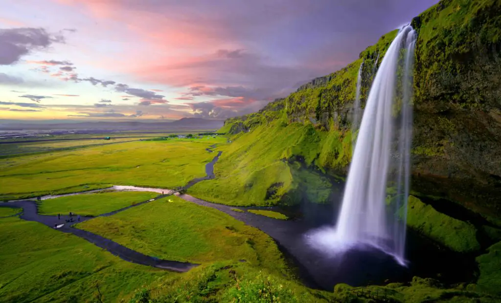 Waterfall in Iceland with green grass and midnight sun